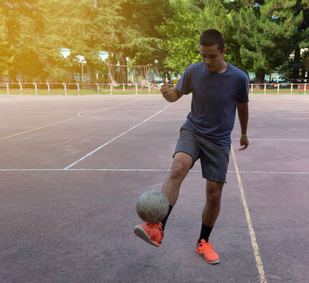 jonge man maakt aanrakingen met de voetbal en tilt het van de grond in een openlucht park - Foto, afbeelding