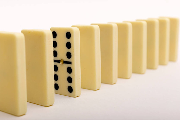 Un domino che si staglia dalla fila. Pietre domino su sfondo bianco. Immagine ad alta ripresa. - Foto, immagini