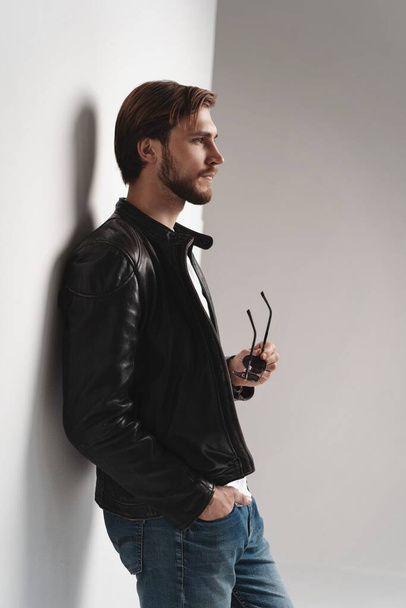 Fashion man, Handsome serious beauty male model portrait wear leather jacket, young guy over white background. - Фото, изображение