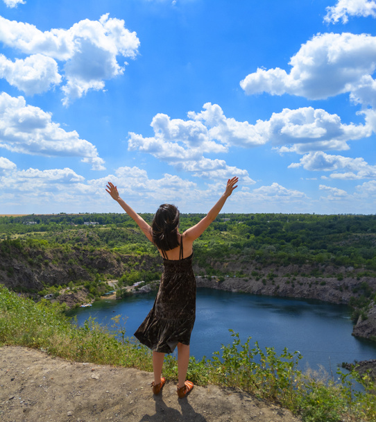 Молода жінка одягнена з відкритими руками вгору стоїть на пагорбі над мальовничим озером. Концепція свободи. Стокова фотографія
. - Фото, зображення