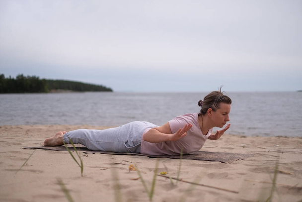 Biała kobieta ćwiczy jogę, uprawia Salabhasana pozować odmiany na plaży - Zdjęcie, obraz