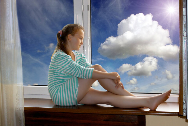 Sny z dzieciństwa. Nastoletnia dziewczyna siedzi na parapecie i śni. Za oknem widać niebo i piękne chmury. - Zdjęcie, obraz