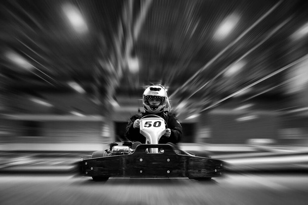 Adam kapalı alanda karting pistinde go-kart 'a gidiyor. siyah ve beyaz görüntü. Kask takıyor.. - Fotoğraf, Görsel