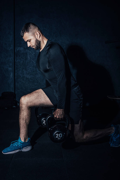 Athletic white man doing squats while lifting kettlebells. Young muscular man doing exercises with kettlebell in gym. Weightlifting workout. Sports, fitness concept. High resulotion image. - Photo, Image