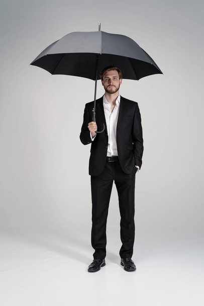 Businessman in a suit standing under black umbrella. - Foto, Imagem
