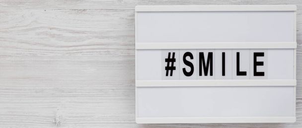 'Glimlach' woord op een lichtbak op een witte houten achtergrond, bovenaanzicht. Vlak gelegen, van boven, boven. Kopieerruimte. - Foto, afbeelding