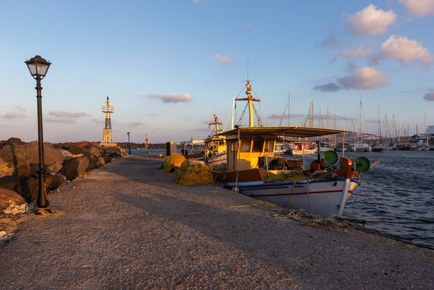 Santorini, Marina Exomitis, un barco pesquero amarrado en un muelle de piedra en el puerto de Vlychada iluminado por los rayos del sol de la mañana. Hay una lámpara en el muelle y un faro de metal en el backgrou
 - Foto, imagen