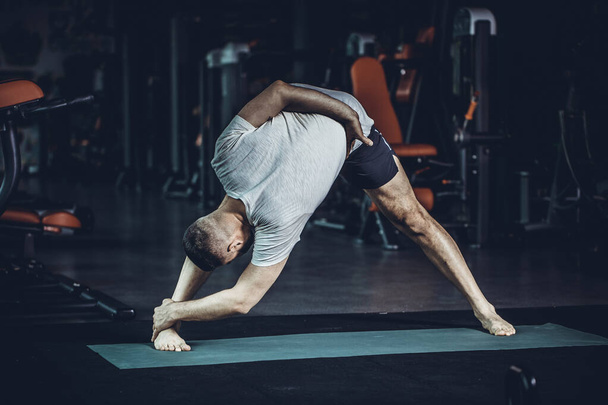 Sportif genç adam yoga yapıyor, esneme egzersizleri yapıyor, üçgen pozlar veriyor esnek omurga için utthita trikonasana asana ve spor salonundaki stresi azaltıyor. Yüksek resulotion resmi. - Fotoğraf, Görsel