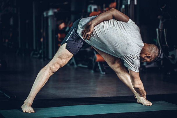 Sporty bearded young man practicing yoga, doing stretching exercise, extended triangle pose, utthita trikonasana asana for flexible spine and relieving stress at gym. High resulotion image. - Photo, Image