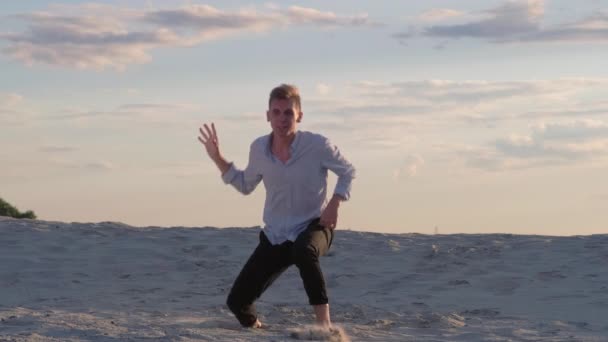 Αισθησιακό νεαρό άνδρα εκτελεί σύγχρονη χορογραφία στην άμμο στο ηλιοβασίλεμα σε ένα όμορφο καλοκαιρινό βράδυ. Πλάνα αργής κίνησης - Πλάνα, βίντεο