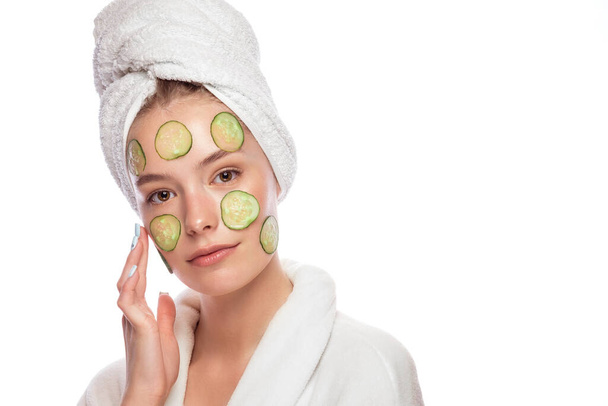 Beautiful tender young girl in a white towel with clean fresh skin posing in front of the camera with a mask of cucumbers on the face. Beauty face. Skin care. - Foto, Imagen