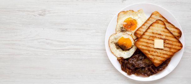 Hausgemachtes gesundes Sunnyside Eggs Frühstück auf einem weißen Teller auf einer weißen Holzoberfläche, Draufsicht. Flach liegend, über Kopf, von oben. Kopierraum. - Foto, Bild