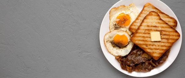 Hausgemachtes gesundes Sunnyside Eggs Frühstück auf einem weißen Teller auf einer grauen Oberfläche, Draufsicht. Kopierraum.  - Foto, Bild
