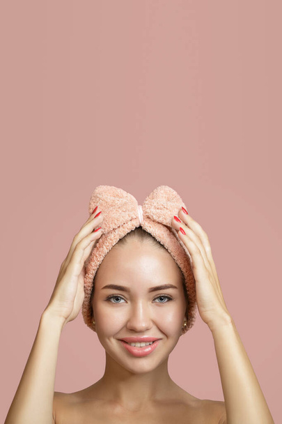 Ικανοποιημένο χαμόγελο μιας νεαρής γυναίκας με καθαρό δέρμα και επίδεσμο στο κεφάλι. Η έννοια της φροντίδας του δέρματος. Αντιγραφή ροζ φόντου - Φωτογραφία, εικόνα
