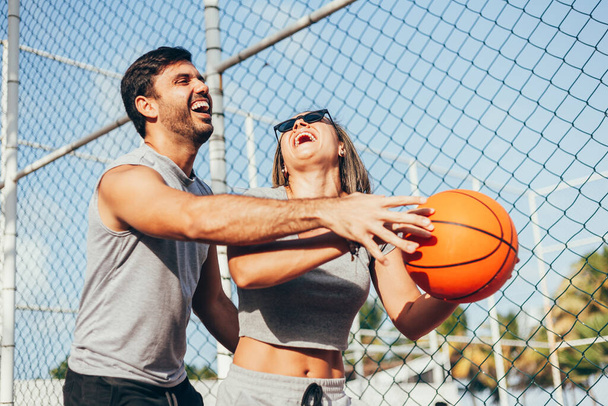 Couple having fun playing basketball outdoors on sunny day. - Foto, afbeelding