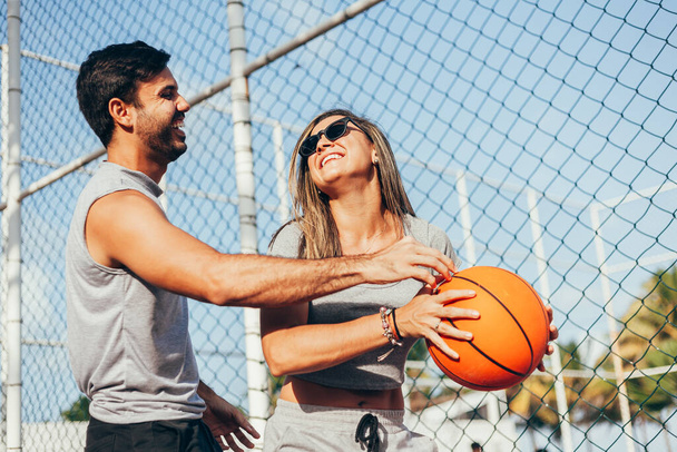 Couple having fun playing basketball outdoors on sunny day. - 写真・画像