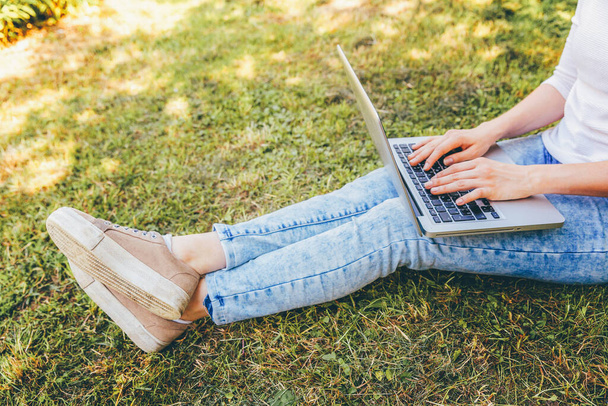 Freelance business concept. Vrouw benen op groen gras gazon in het stadspark, handen werken op laptop pc computer. Lifestyle authentieke openhartige student meisje studeren buiten. Mobiel kantoor - Foto, afbeelding