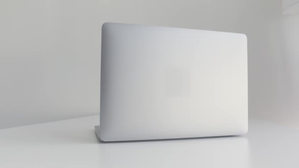 Zadní pohled na bílý notebook izolovaný na bílém pozadí. Akce. Moderní štíhlý design nového notebooku z hliníkového materiálu na bílém stole, koncepce moderních technologií. - Záběry, video
