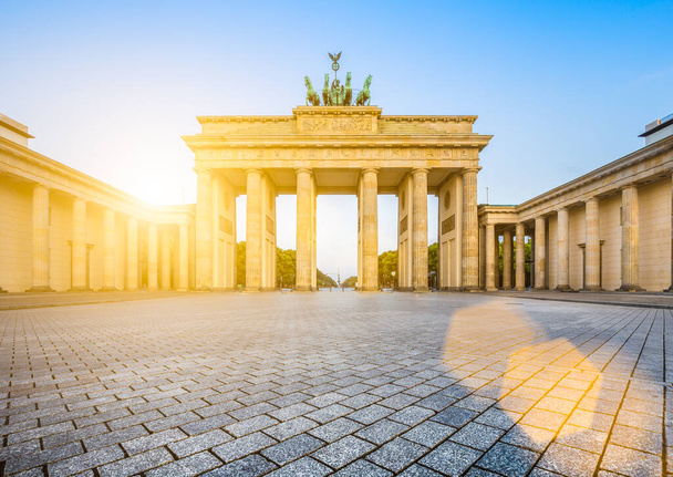 Słynny Brandenburger Tor (Brama Brandenburska), jeden z najbardziej znanych zabytków i symboli narodowych Niemiec, w pięknym złotym świetle poranka o wschodzie słońca z efektem flary obiektywu, Berlin, Niemcy - Zdjęcie, obraz