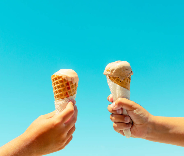 Couple kids hands holding ice cream cones against blue sky background in summer vacation. Summer food, summertime joy, vacation, holidays - Fotografie, Obrázek
