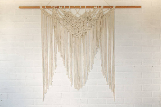 Beige reed against a white wall with a macrame wall panel. A minimal, stylish, trendy concept with a beautiful background with light neutral colors. - 写真・画像