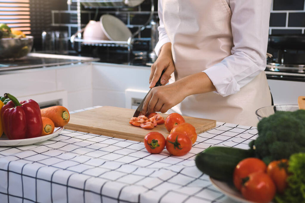 Kobieta z nożem i rękami krojącymi pomidory na drewnianej desce w kuchni. - Zdjęcie, obraz