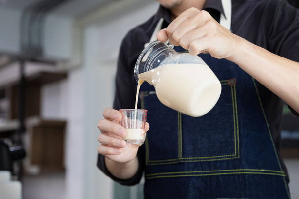 Barista wearing apron measuring milk for mixed coffee in coffee shop. - 写真・画像