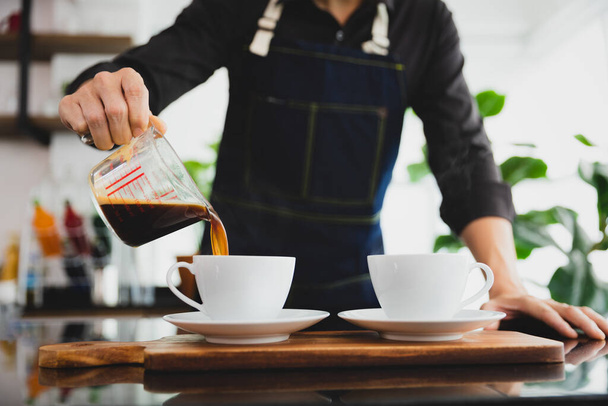 Barista gießt schwarzen Kaffee in weiße Tasse für den Service im Coffeeshop. - Foto, Bild