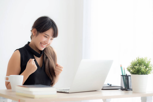 Hermoso retrato asiática joven sonrisa trabajo ordenador portátil en línea con feliz satisfecho sentado en la oficina del escritorio, chica usando portátil con emocionado y contento, negocio y el concepto de éxito
. - Foto, imagen