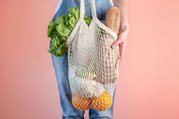 A modern woman in jeans is holding a string bag with purchases. Concept of eco-friendly behavior, the use of reusable bags and concern for the environment - Foto, Imagem