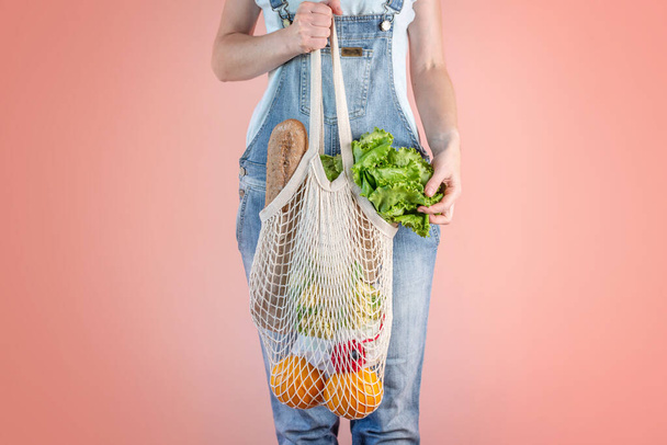 A modern woman in jeans is holding a string bag with purchases. Concept of eco-friendly behavior, the use of reusable bags and concern for the environment - Фото, изображение