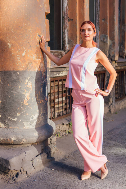 Young woman wearing pink suit and shoes witjh high hills posing on the street next to the old building during sunset - 写真・画像