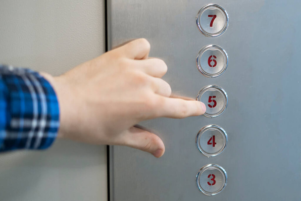 eine Hand aus nächster Nähe, die einen Knopf in der Fahrstuhlkabine drückt - Foto, Bild