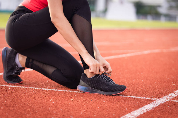 市内スタジアムでのジョギングワークアウトの前に、女性運動選手のランナーのネクタイの靴を閉じます。健康と関係のストックフォト. - 写真・画像