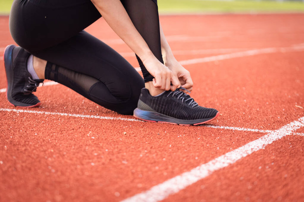 市内スタジアムでのジョギングワークアウトの前に、女性運動選手のランナーのネクタイの靴を閉じます。健康と関係のストックフォト. - 写真・画像