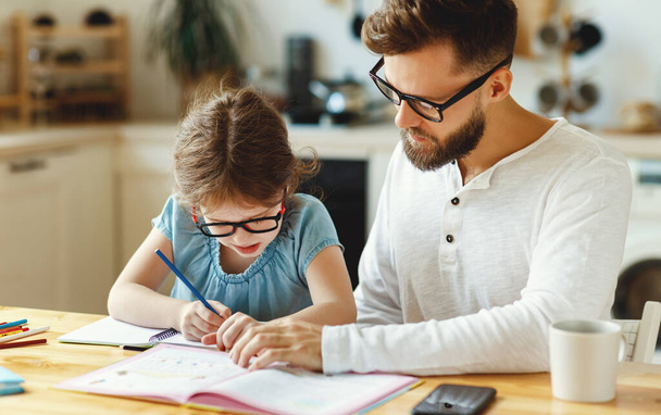 Keskittynyt nuori mies istuu lähellä pientä tytärtä ja selittää vaikeaa tehtävää auttaen samalla kotitehtäviä kotona opiskelun aikana. - Valokuva, kuva