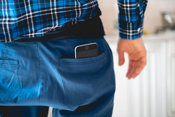 ένα κοντινό smartphone μέσα στην τσέπη των ανδρικών ρούχων, πίσω όψη, ως σύμβολο των επιπτώσεων στην υγεία από το κινητό τηλέφωνο - Φωτογραφία, εικόνα