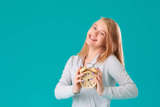 Cute laughing positive girl in sports clothes holding an alarm clock. Turquoise background - Photo, image