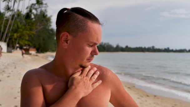 Jóképű fiatalember megérinti meleg bőr éget a vállán a napsütéses napon - Felvétel, videó