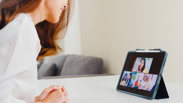Junge asiatische Unternehmerinnen telefonieren per Tablet-Videotelefonie mit der Familie, während sie von zu Hause aus im Wohnzimmer arbeiten. Selbstisolierung, soziale Distanzierung, Quarantäne für Coronavirus im nächsten Normalkonzept. - Foto, Bild