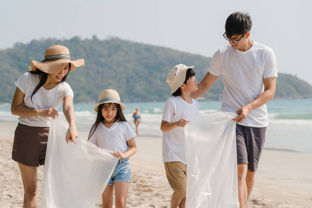 Jóvenes asiáticos felices activistas familiares recogiendo residuos plásticos y caminando por la playa. Los voluntarios asiáticos ayudan a mantener la naturaleza limpia la basura. Concepto sobre problemas de contaminación ambiental de conservación
. - Foto, imagen
