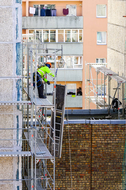 un empleado en equipo de seguridad monta andamios en la fachada de una casa de varios pisos a una altura peligrosa - Foto, Imagen