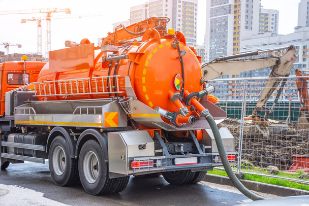 Bombeo de agua de los canales de alcantarillado durante la construcción de carreteras en la ciudad. Camión con tanque de agua naranja
 - Foto, Imagen