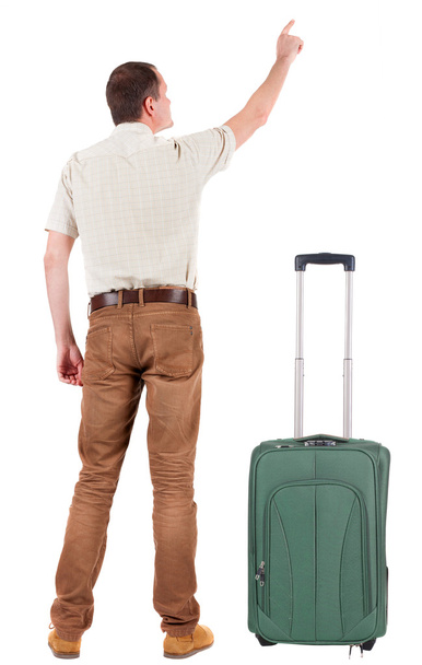Back view of pointing young man traveling with suitcase. - Foto, Bild