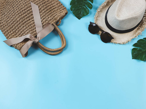 Concept de voyage et vacances d'été, accessoires de vacances pour femmes (sac tissé, chapeau et lunettes de soleil) sur fond bleu avec feuilles de monstère tropicale.. vue du dessus avec espace de copie. - Photo, image