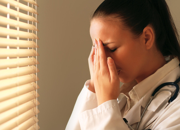 Female doctor with head pain standing near window - 写真・画像