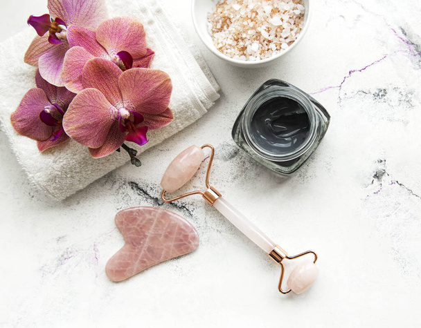 Rotina de beleza da manhã Skincare no banheiro em casa - massageador de rolo de jade facial para terapia cosmética de bem-estar, máscara e flores de orquídeas no fundo de mármore - Foto, Imagem