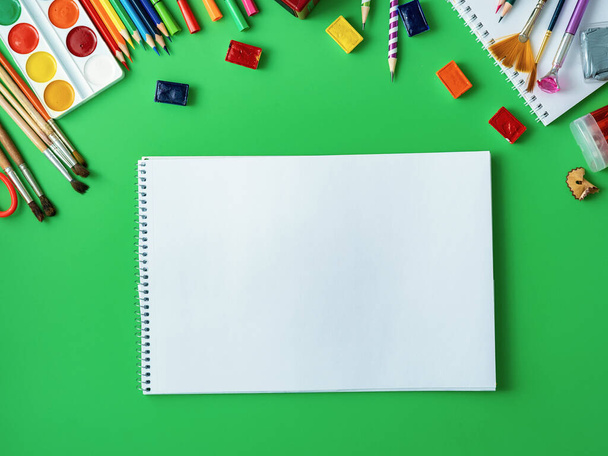 School supplies are displayed on a green background. In the center, on a green surface, is an album, a place to copy space. Watercolors, pencils, markers, brushes, and drawing supplies.Back to school. - Fotografie, Obrázek
