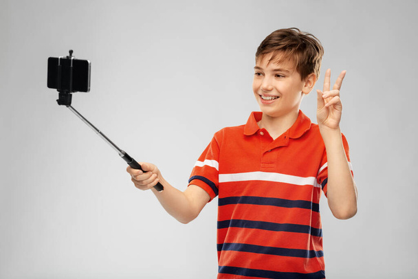 boy taking picture with smartphone on selfie stick - Zdjęcie, obraz