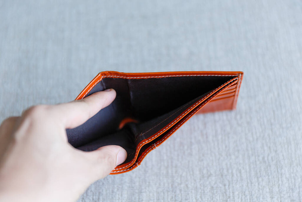 Человек открывает пустой оранжевый кожаный бумажник, потому что его уволили с работы, так что он не в состоянии оплатить кредит и ипотеку. - Фото, изображение